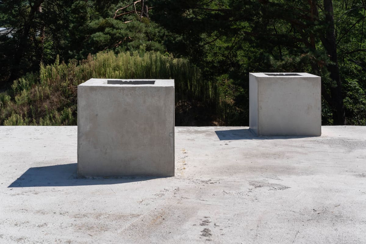 Zwei Betonwürfel mit dunklen Öffnungen stehen auf der nackten Dachplatte eines Erdhauses vor der Erdüberdeckung.