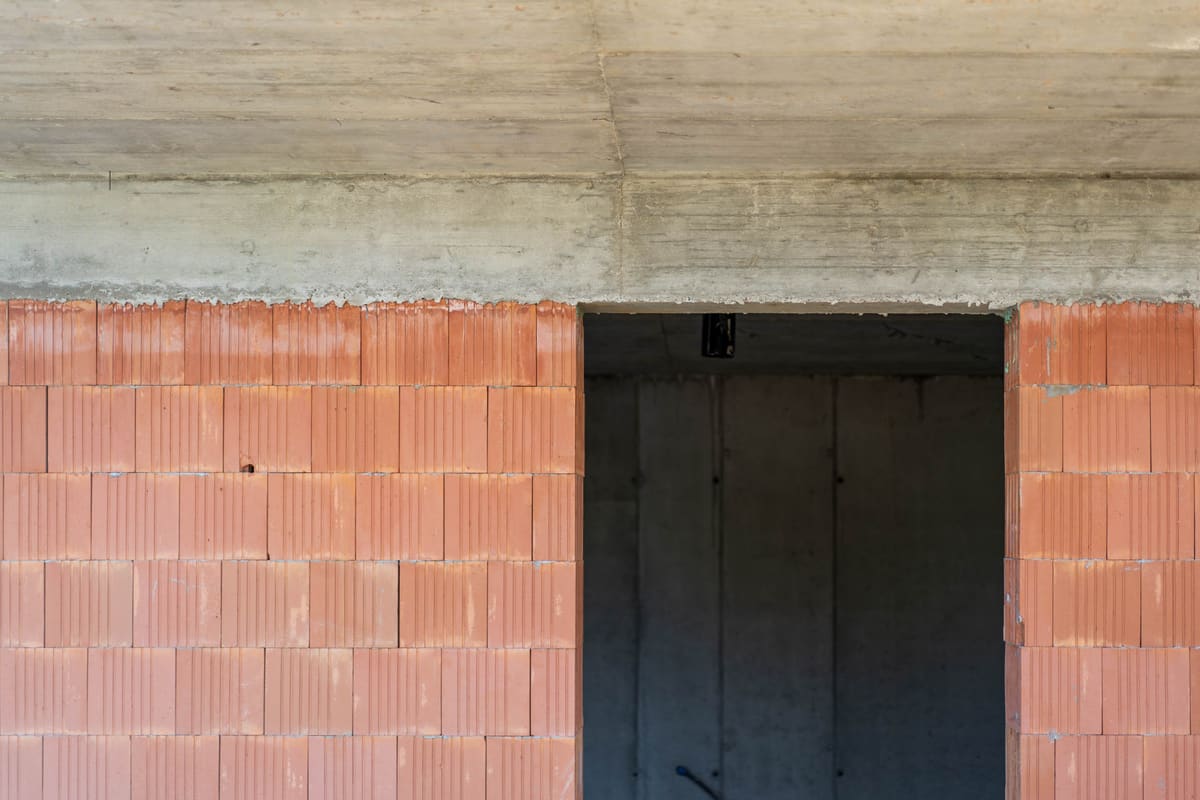 Baudetail eines Erdhauses: Ziegelhohlblockwand unter roher Betondecke, dahinter eine dunkle Türöffnung.