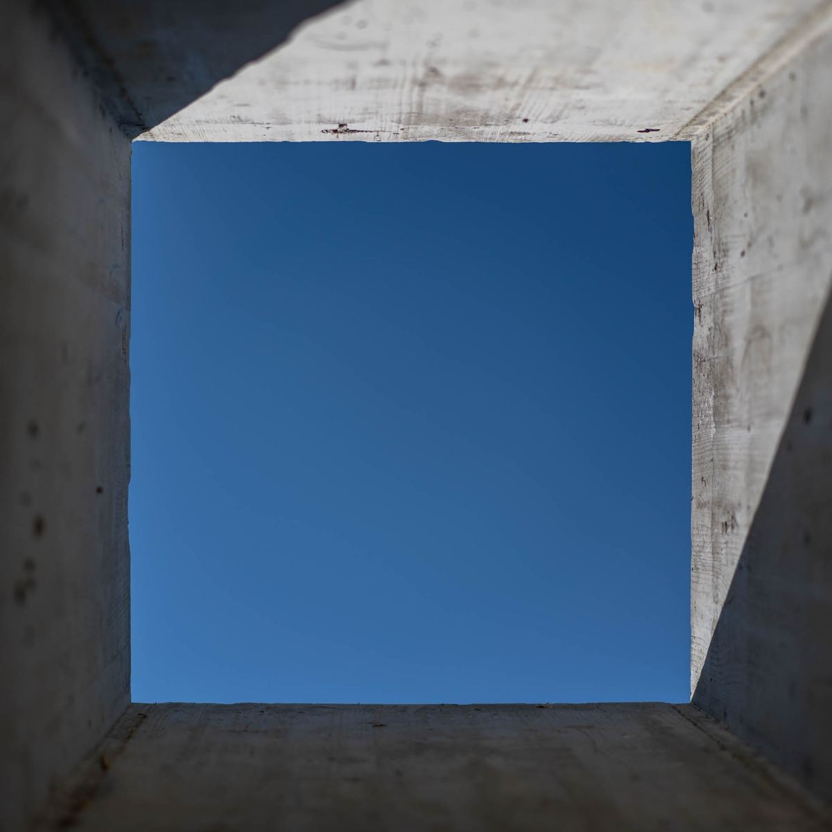Quadratische Betonöffnung an einem Erdhaus, Schalungsstruktur sichtbar, dahinter ein Stück blauer Himmel