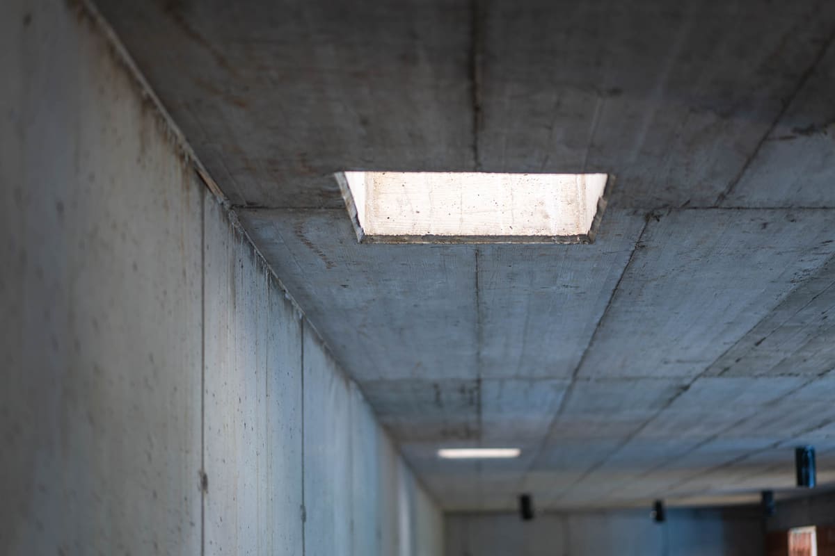 Roher Betonkorridor eines Erdhauses, Schalungsspuren an Decke und Wand, Tageslicht durch eine Deckenöffnung