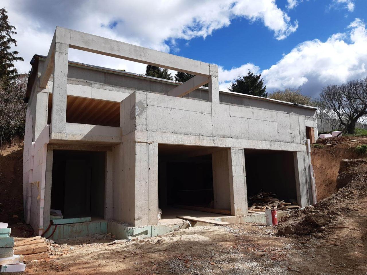 Rohbau eines Erdhauses im Hang, unverputzte Betonwände, offene Fenster- und Türöffnungen und Dämmplatten an einer Wand.