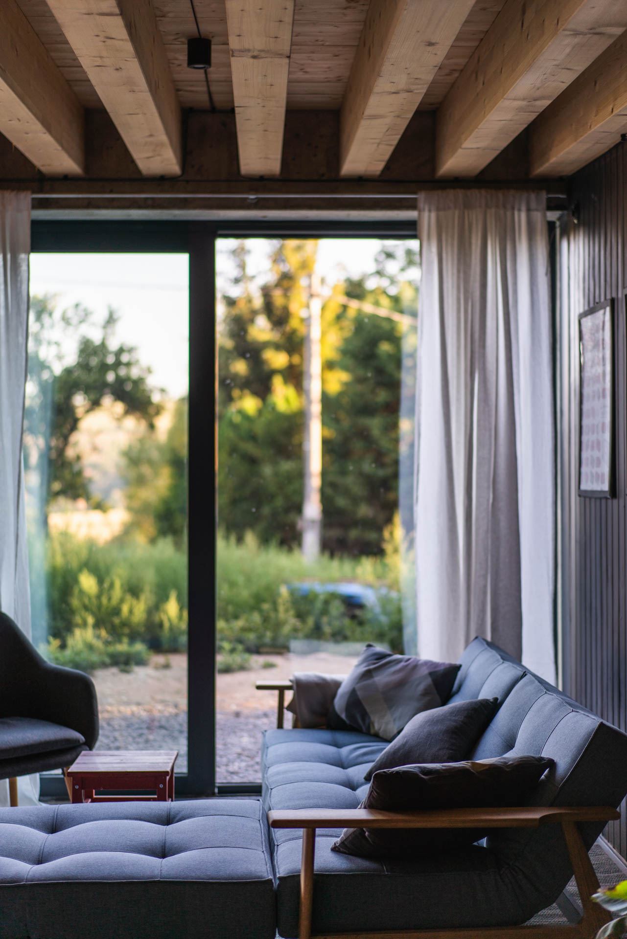 Living room of the earth-sheltered house in Banska Stiavnica, grey sofa facing a sliding glass wall to the garden