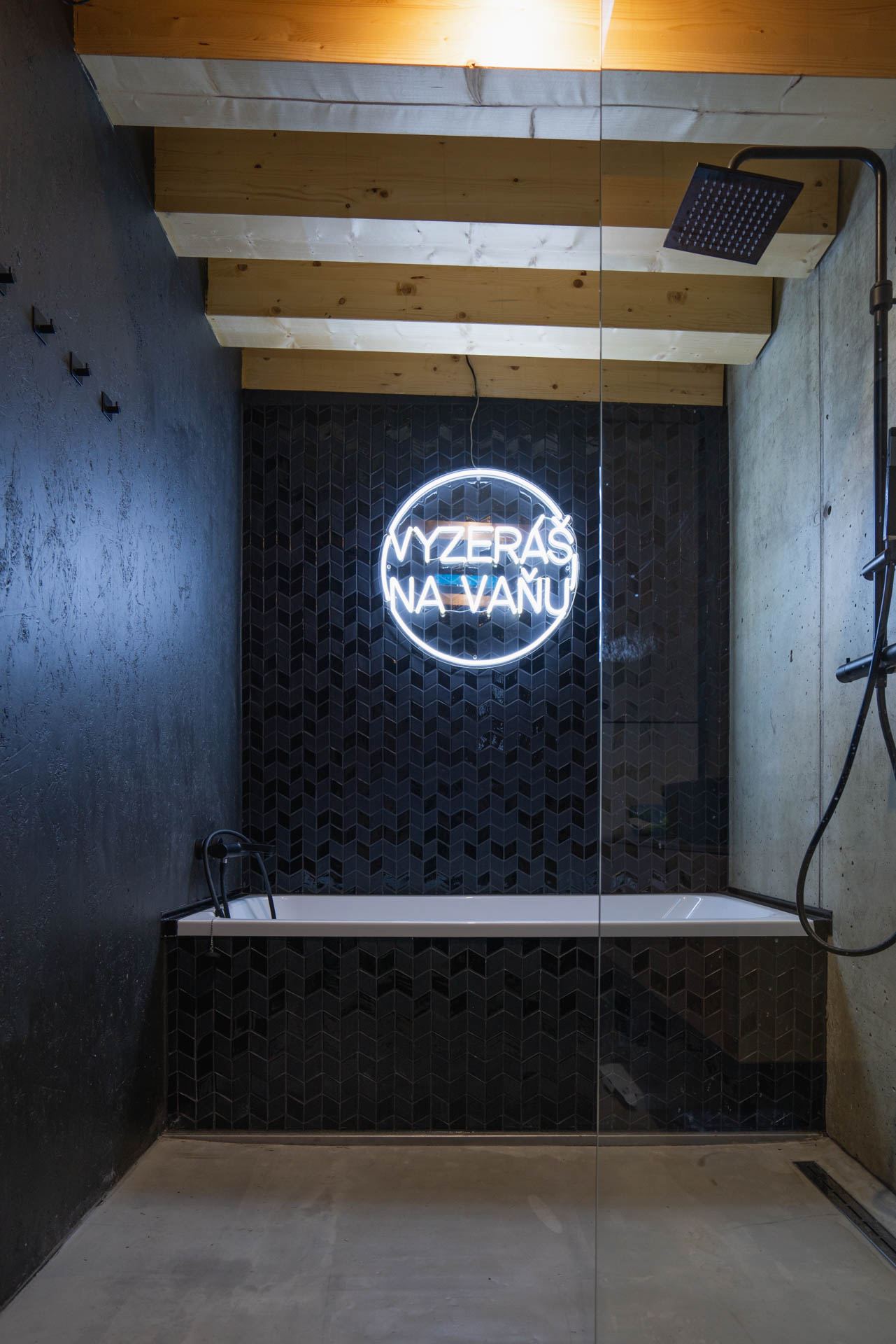 Bathroom of the earth-sheltered house in Banská Štiavnica, chevron-tiled tub wall, neon sign, concrete floor