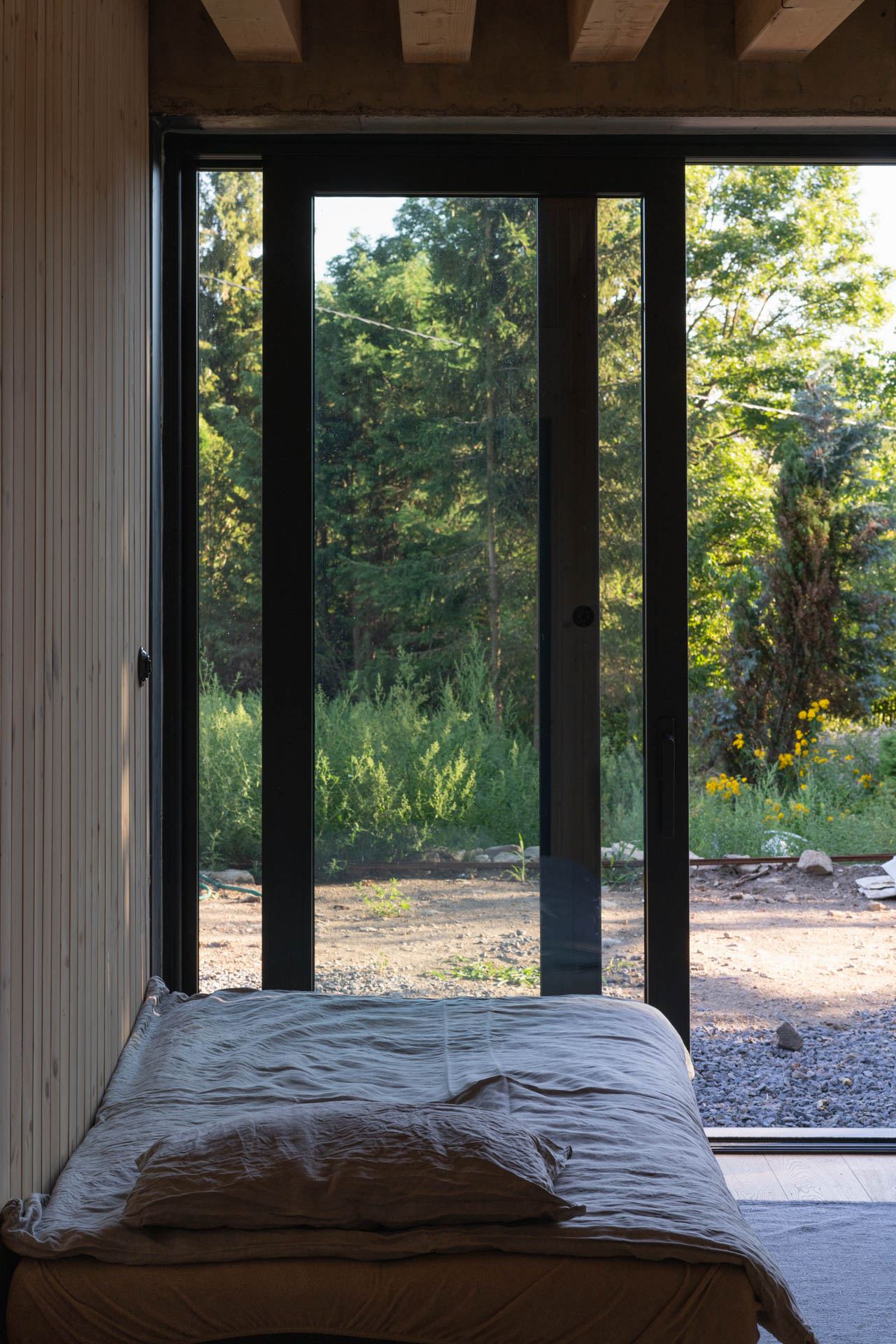 Bedroom with timber-clad walls and beamed ceiling in the Banska Stiavnica earth-sheltered house, glazed doors open to greenery