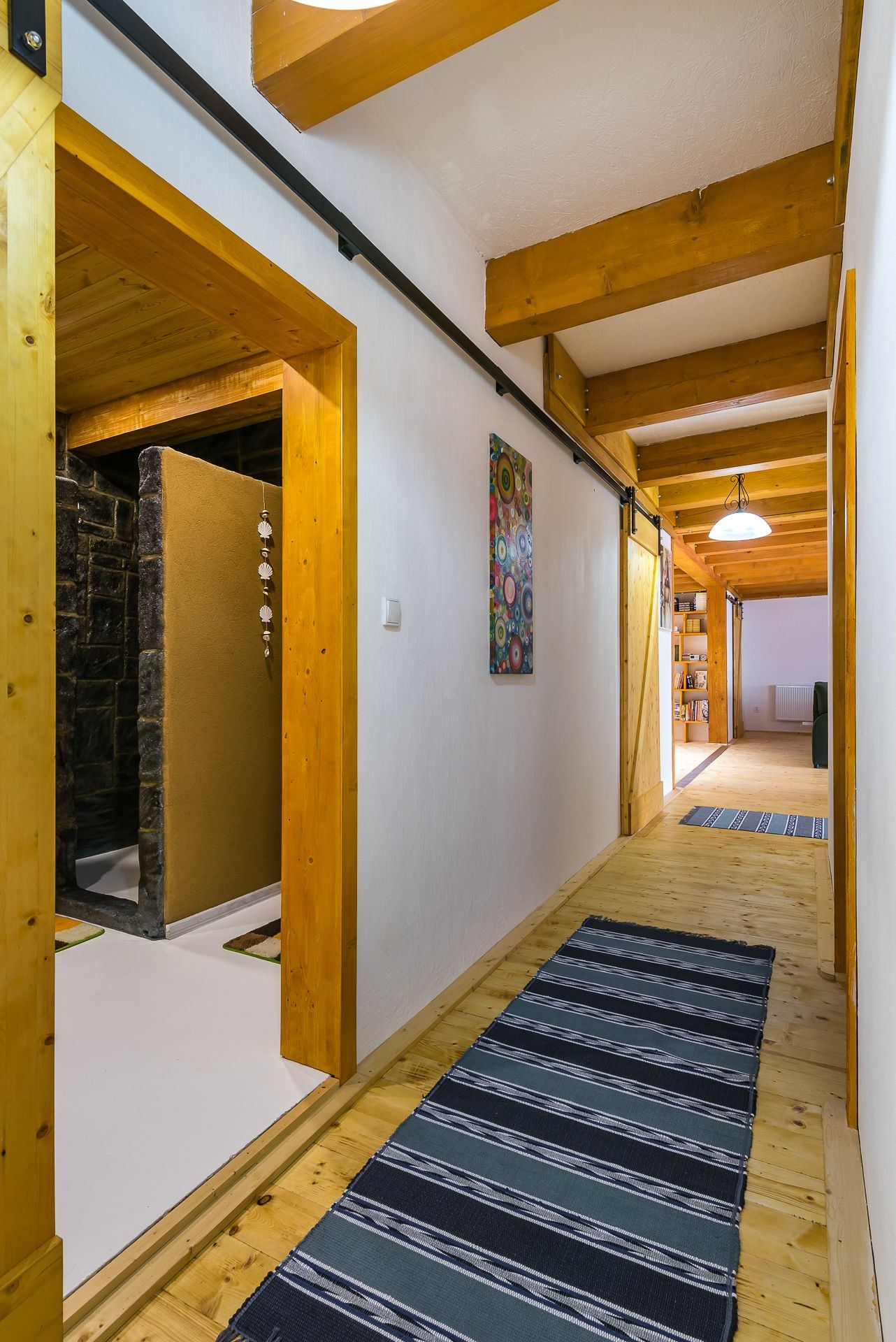 Hallway in the Zemplin earth-sheltered house, wood-beam ceiling, sliding barn door and stone-tiled shower alcove