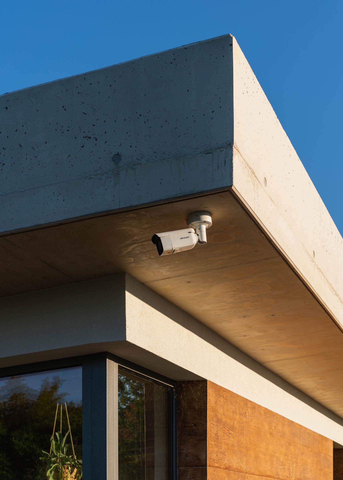 Concrete roof overhang of an earth-sheltered house in Nove Mesto nad Vahom, security camera under eave, glazed corner window below.