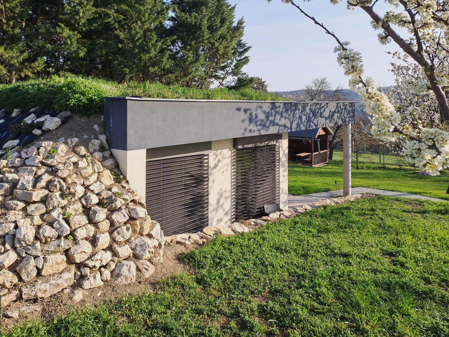 Casa interrata Balaton nel pendio con tetto verde, persiane chiuse, muro in pietra e terrazza verso le colline.