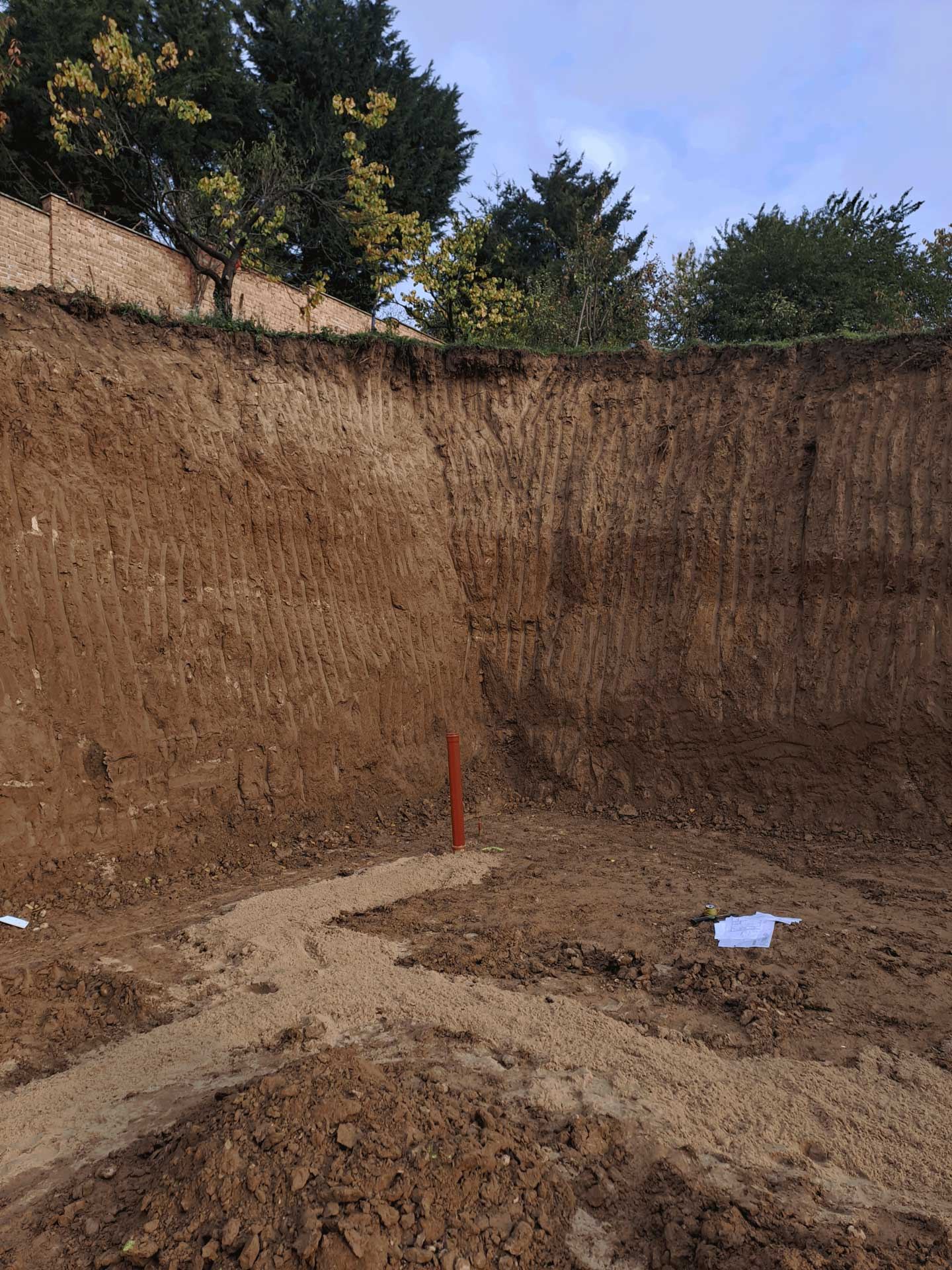 Profondo scavo con pareti di terra segnate dagli attrezzi, tubo arancione sul fondo, preparazione per una casa interrata a Trnava.