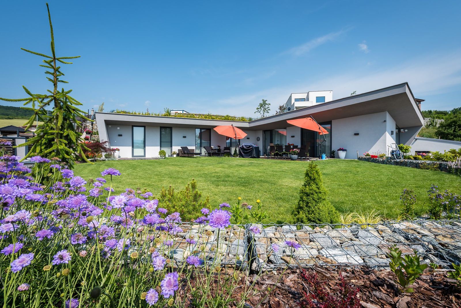 Casa interrata Hoblina a Kosice, facciata vetrata bianca, terrazza con ombrelloni arancioni e tetto inerbito