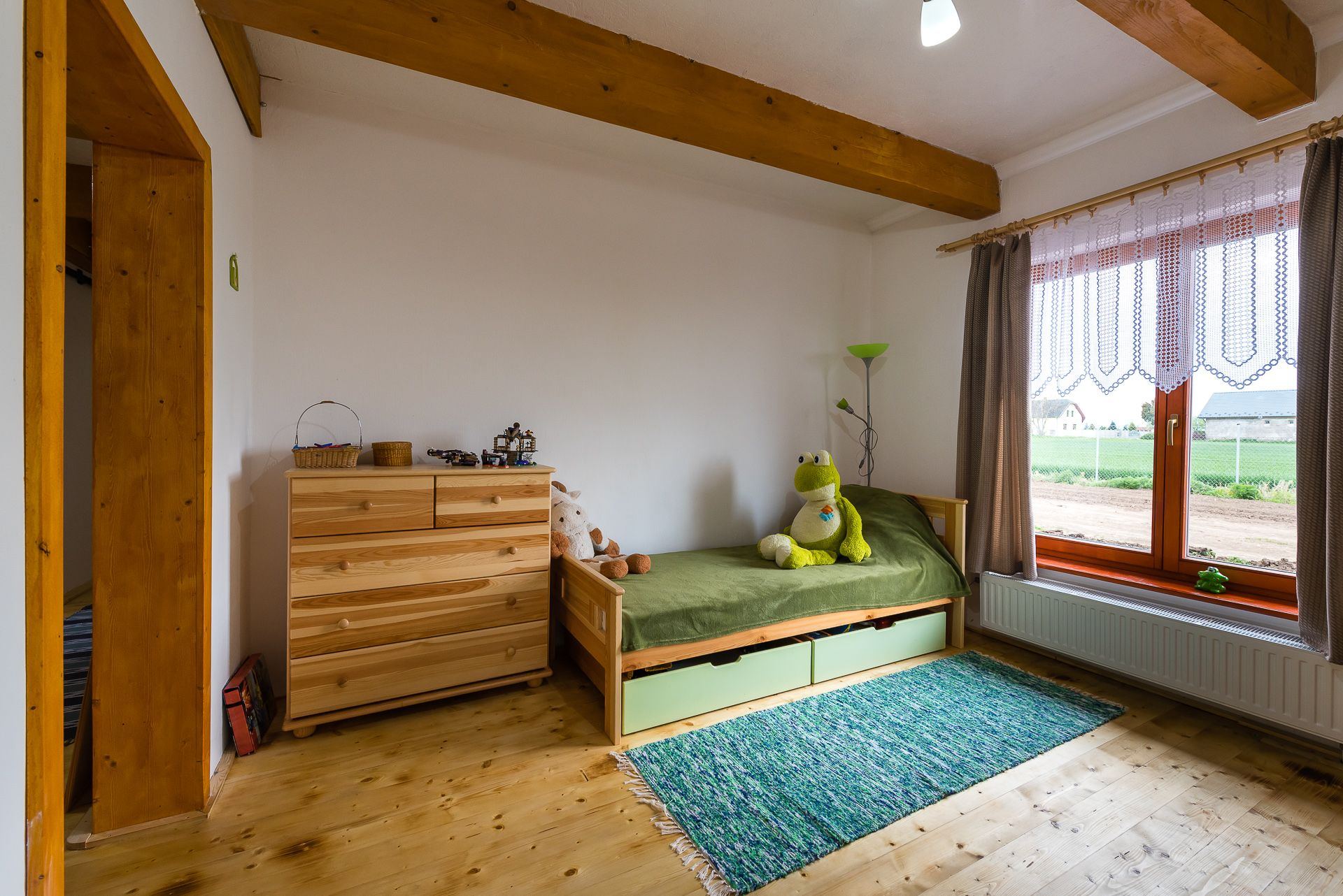 Child's room in the Zemplin earth-sheltered house, wooden bed with stuffed toys under beamed ceiling and a field-view window