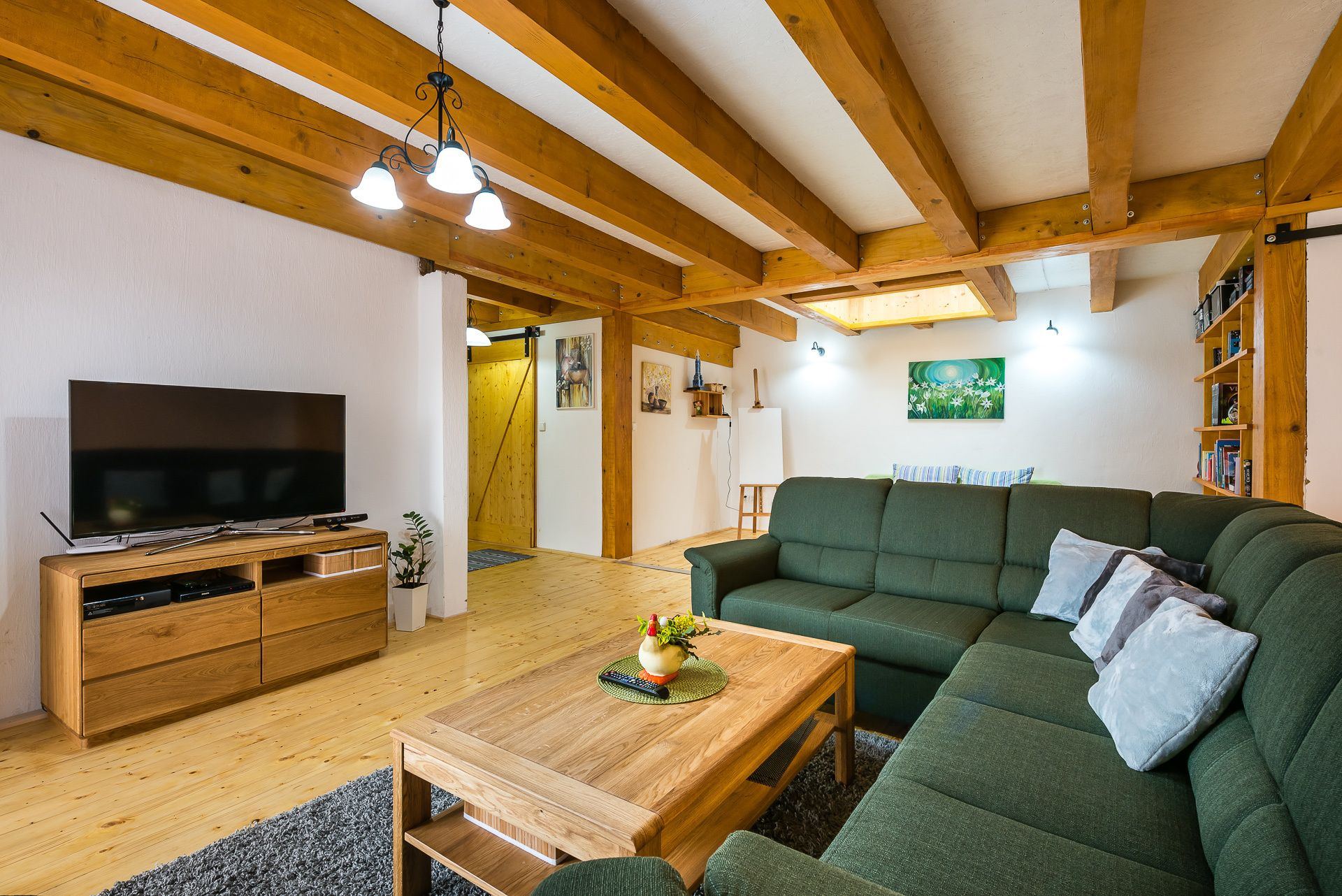 Living room of the Zemplin earth-sheltered house with beamed ceiling, skylight and green sectional sofa