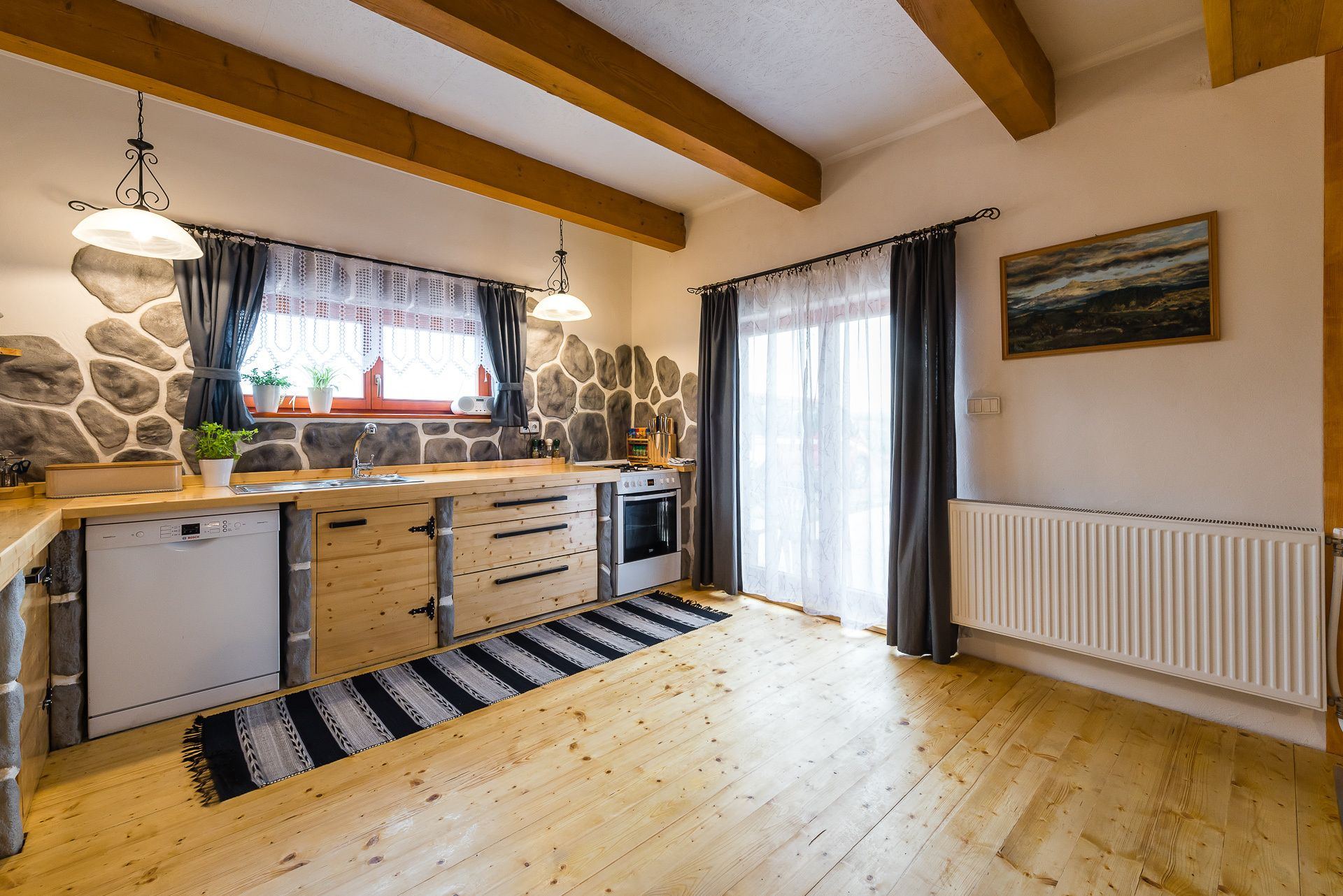 Kitchen in the Zemplin earth-sheltered house with wooden cabinets, stone-pattern wall and exposed ceiling beams