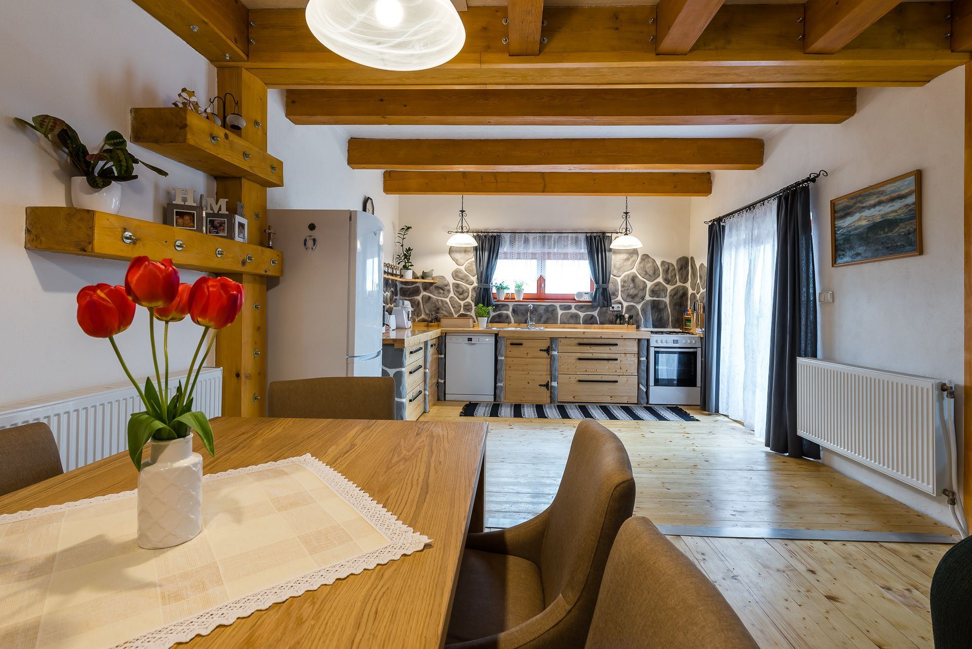 Kitchen and dining area of the Zemplin earth-sheltered house, with wood beams, tulips on the table and pendant lights.