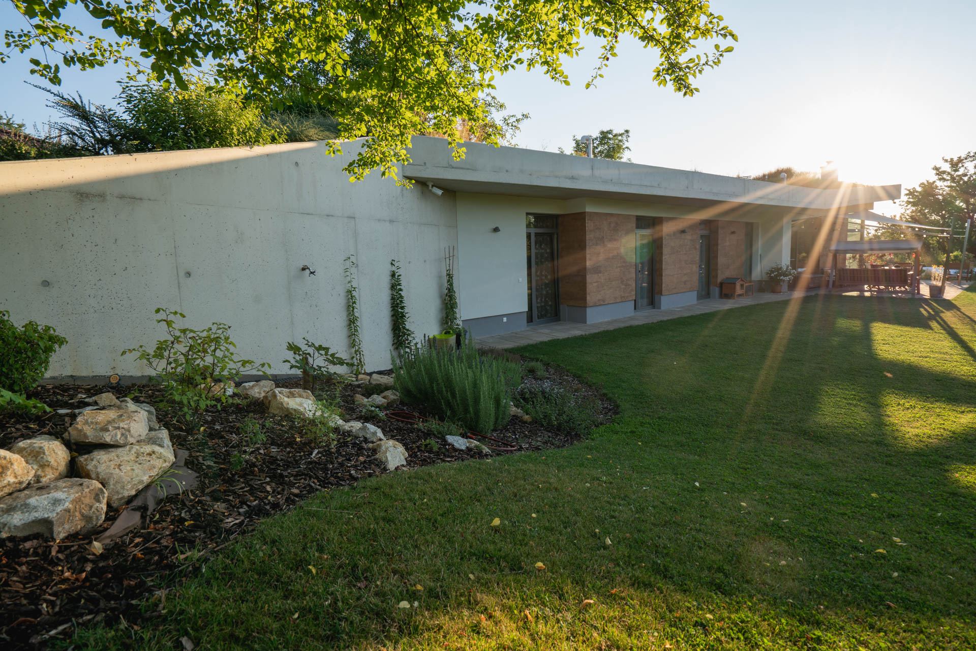 Earth-sheltered house in Nove Mesto nad Vahom, low sun on the glazed front, grass growing over the concrete roof edge.