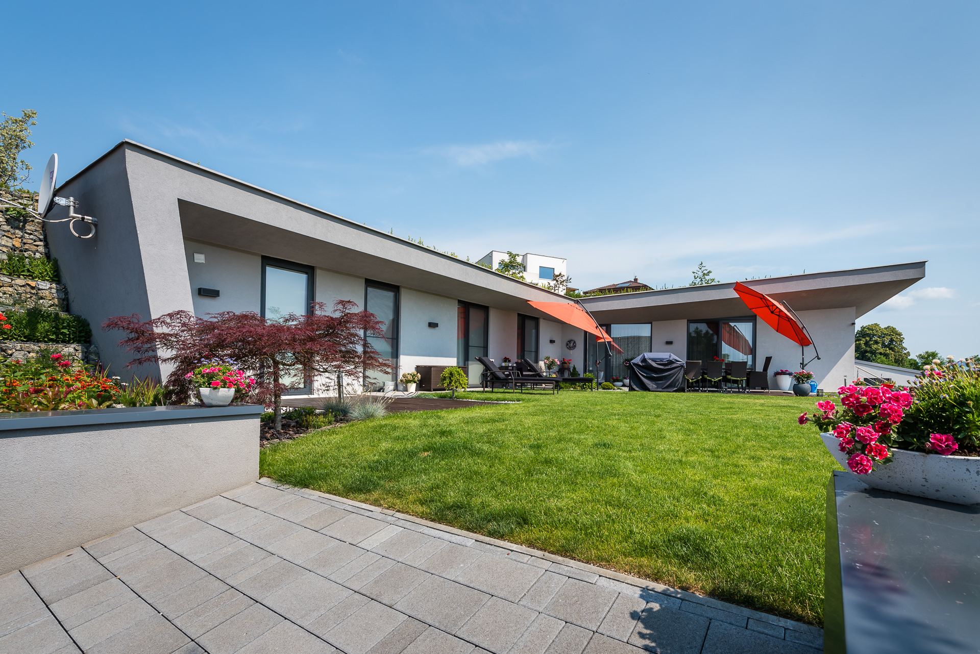 Earth-sheltered house Hoblina in Košice with glazed front, terrace, orange umbrellas and stone retaining wall behind