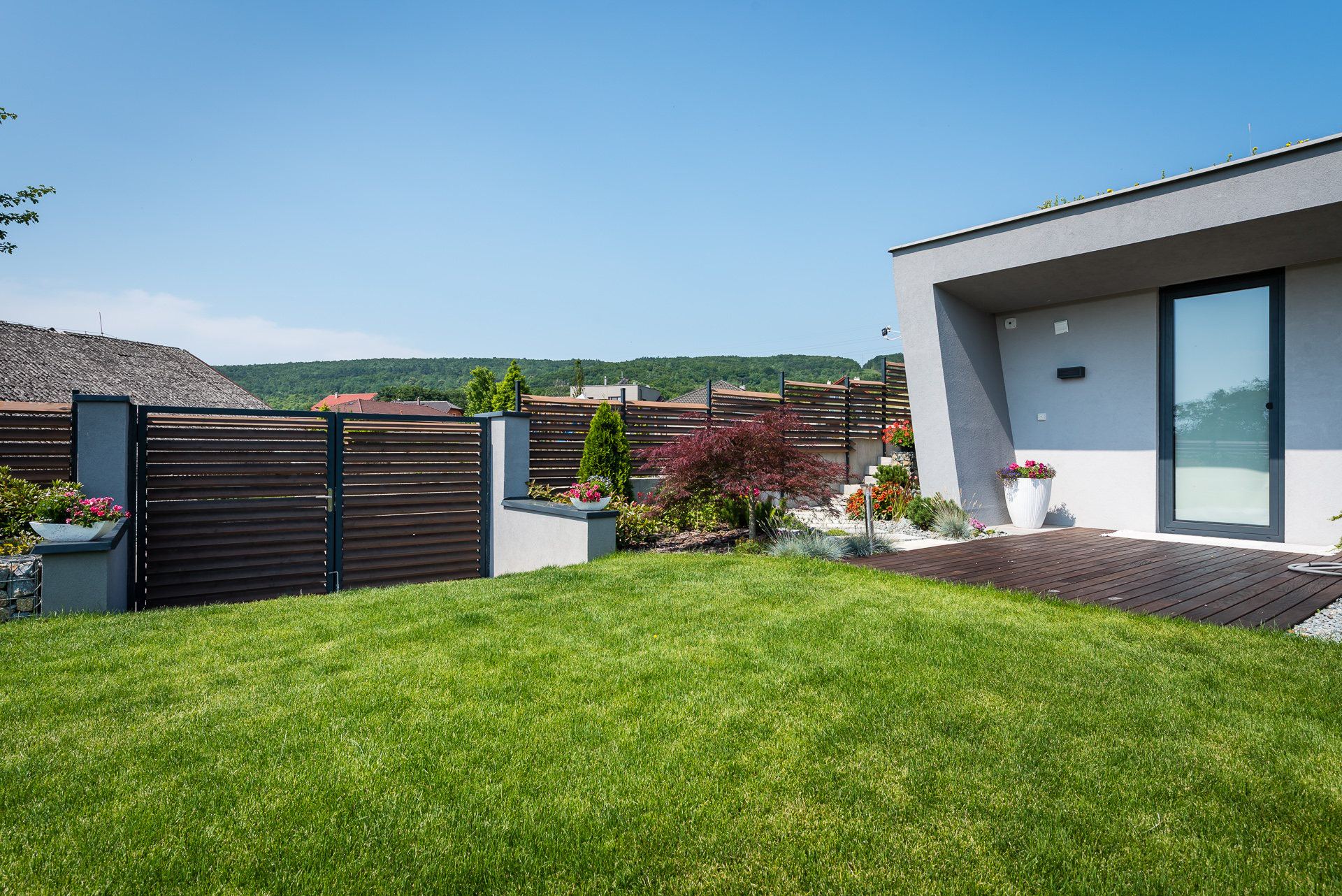 Earth-sheltered house Hoblina in Košice with white angled facade, glass door, wood deck and planted roof edge
