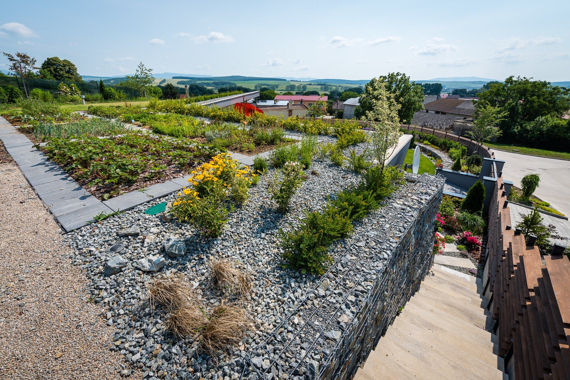 Rooftop garden of the Hoblina earth-sheltered house in Košice, with raised vegetable beds, gravel plantings and gabion walls above a village view.