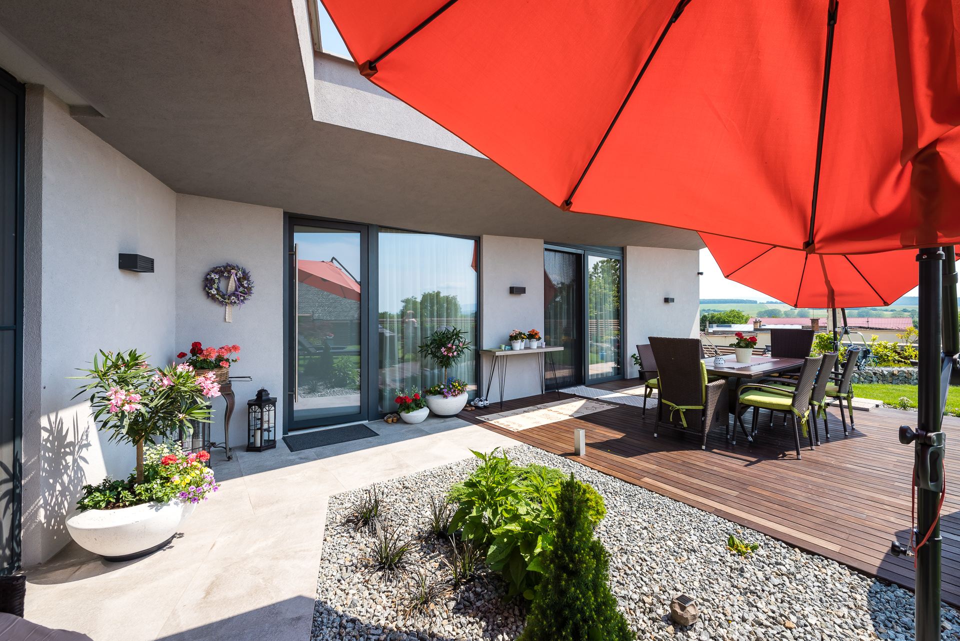 Terrace of the earth-sheltered Hoblina house in Košice, dining table with red umbrella by the glazed facade