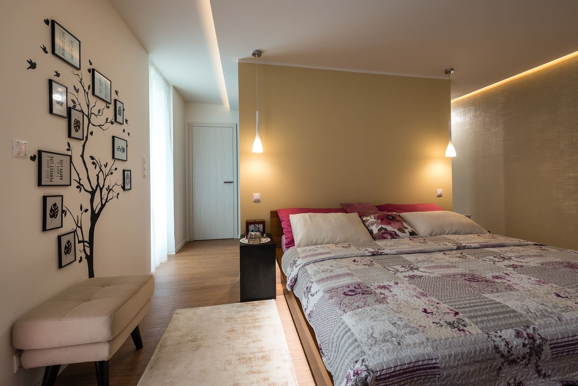 Bedroom of the Hoblina earth-sheltered house in Kosice, mustard wall, patchwork quilt bed and pendant lamps.