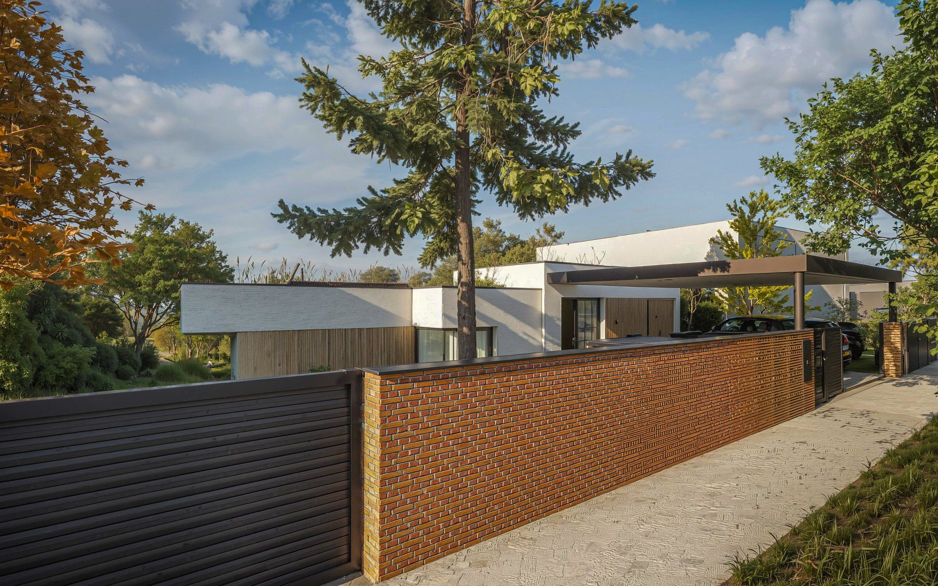 Street view of an earth-sheltered house in Bratislava, white walls and carport behind a brick wall and gate