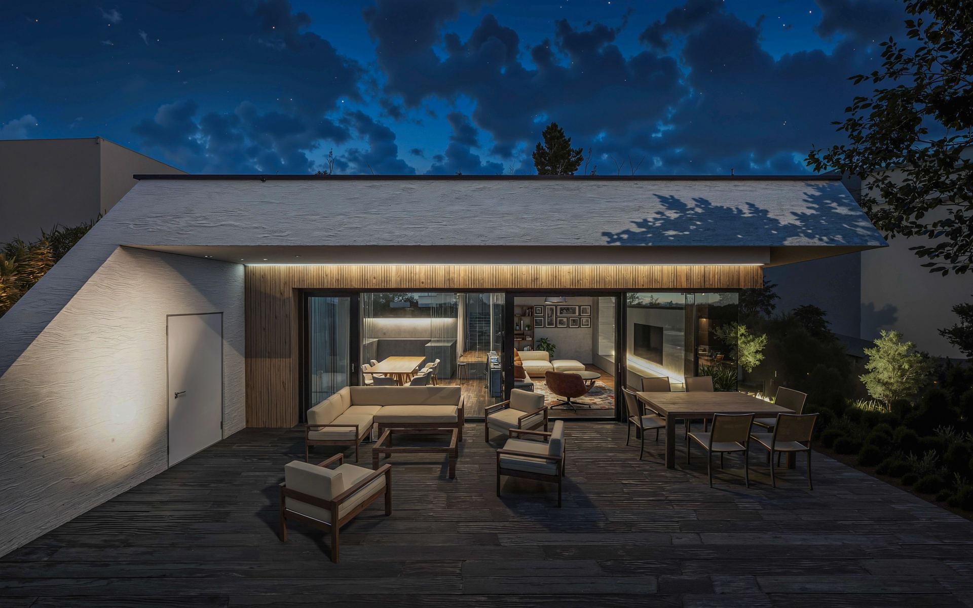 Night view of an earth-sheltered house in Bratislava, glazed front lit up showing dining table and kitchen island, terrace with lounge furniture