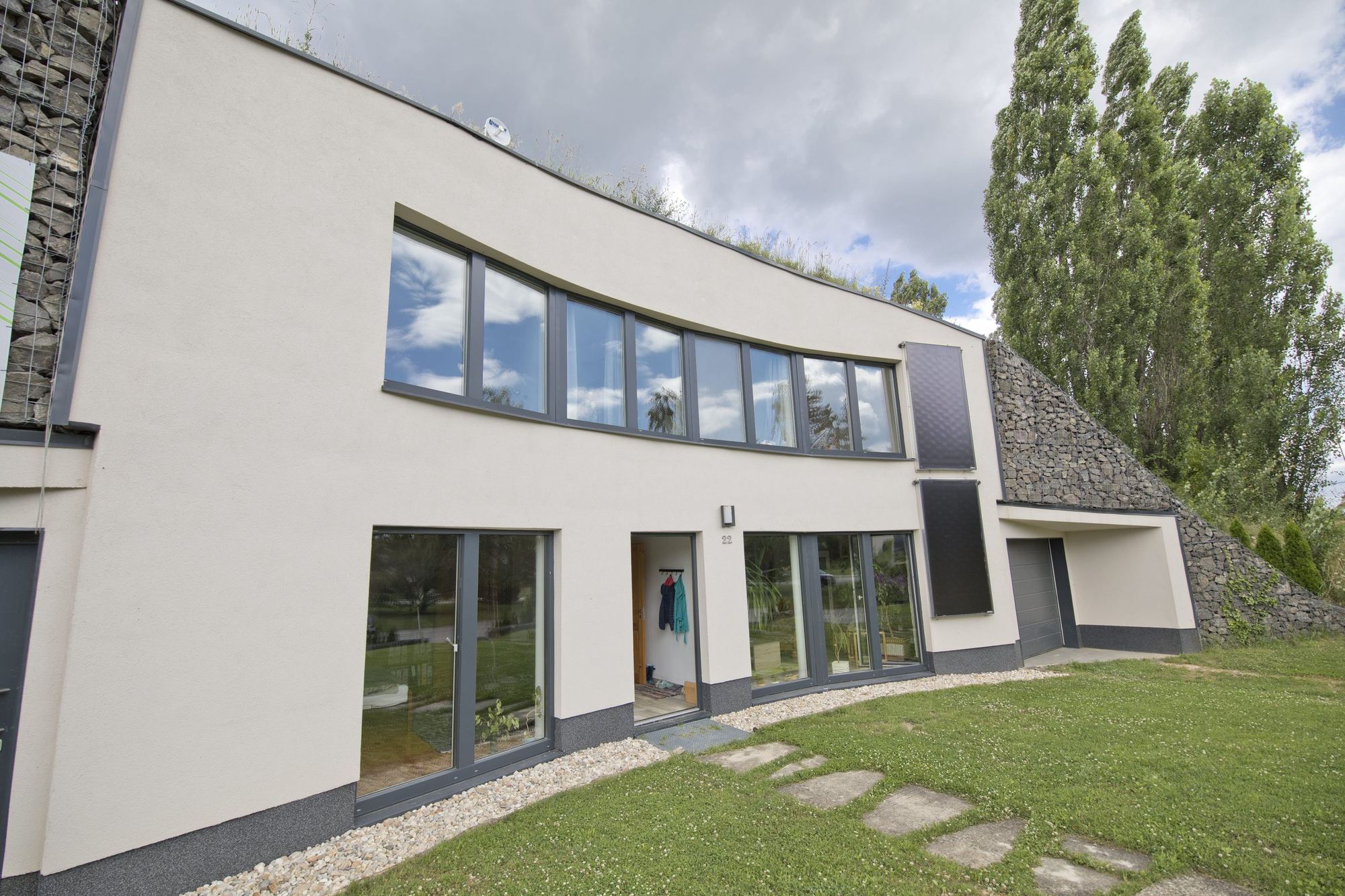 Earth-sheltered house in Rohožník, curved white facade, door 22, solar panels and grassy roof edge