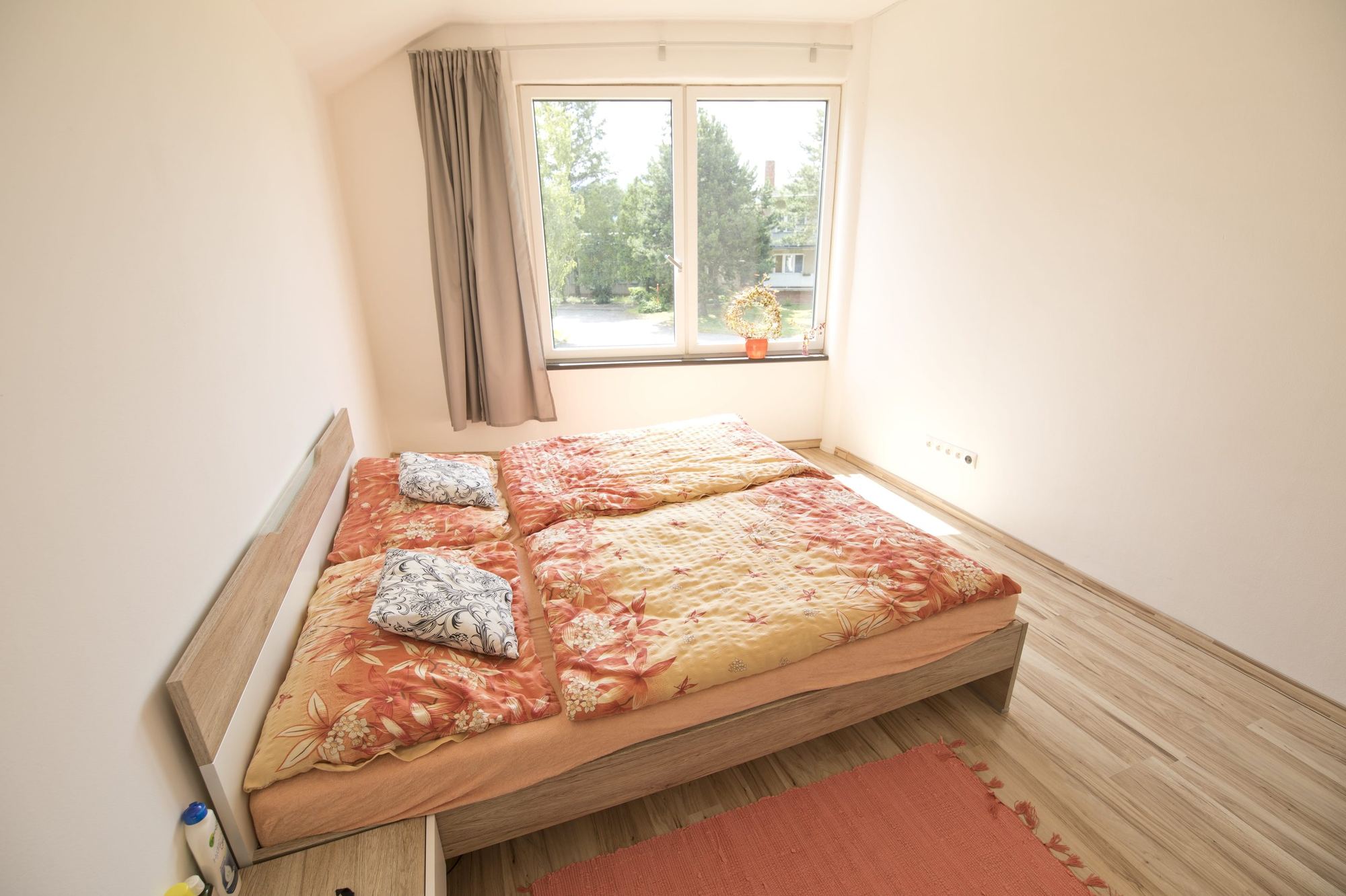 Bedroom of the earth-sheltered house in Rohožník with a sloped window, wooden bed and orange floral duvets