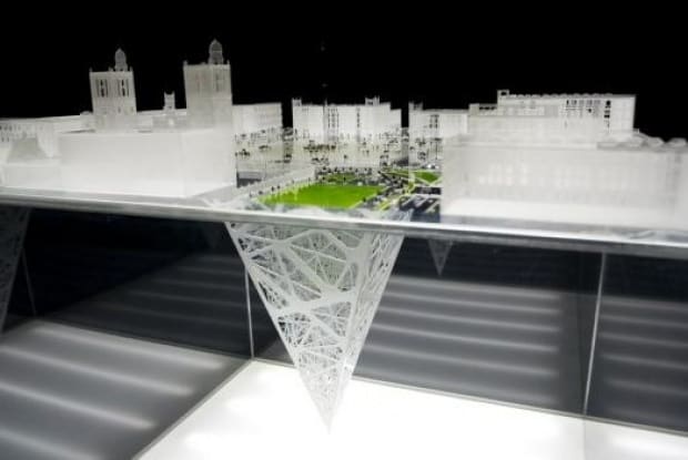 Weißes Architekturmodell einer Stadtansicht mit grünem Park, darunter hängt eine umgekehrte Gitterpyramide