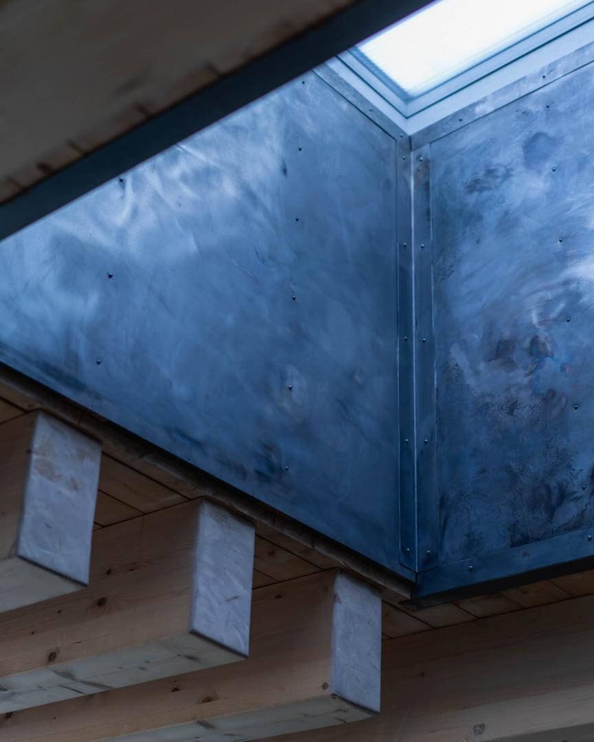 Blick von unten in einen Lichtschacht eines Erdhauses, verschraubte Metallpaneele über sichtbaren Holzbalken.