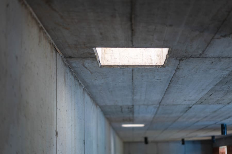 Corridoio grezzo in cemento di una casa interrata, apertura nel soffitto lascia entrare luce prima del lucernario
