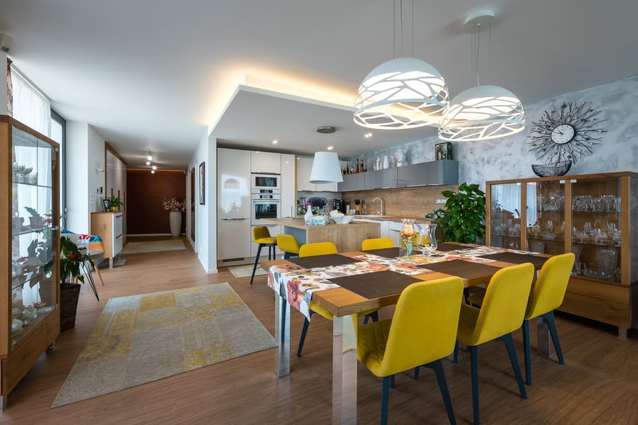 Zona pranzo e cucina della casa interrata Hoblina a Košice, tavolo in legno, sedie gialle, mobili bianchi.