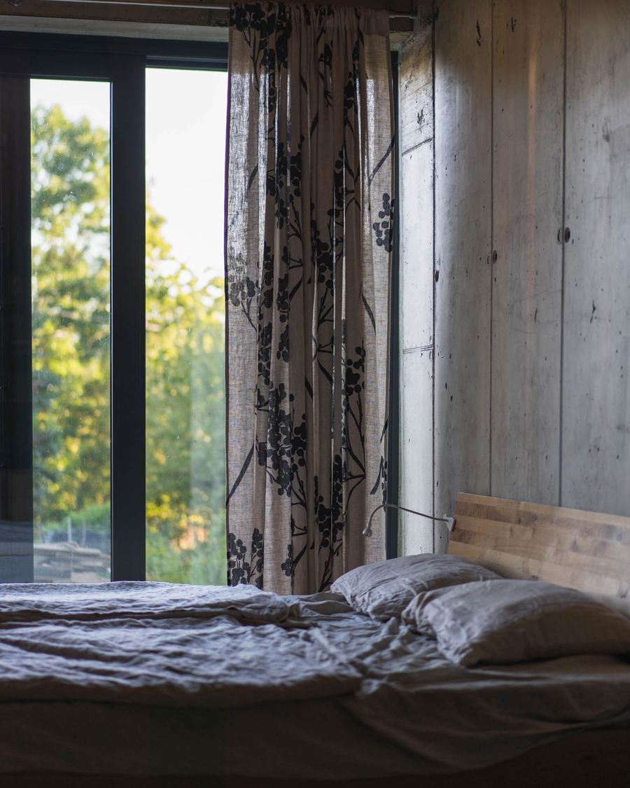 Camera da letto di una casa interrata a Banska Stiavnica, parete in cemento a vista, finestra alta con tenda floreale e vista sul verde